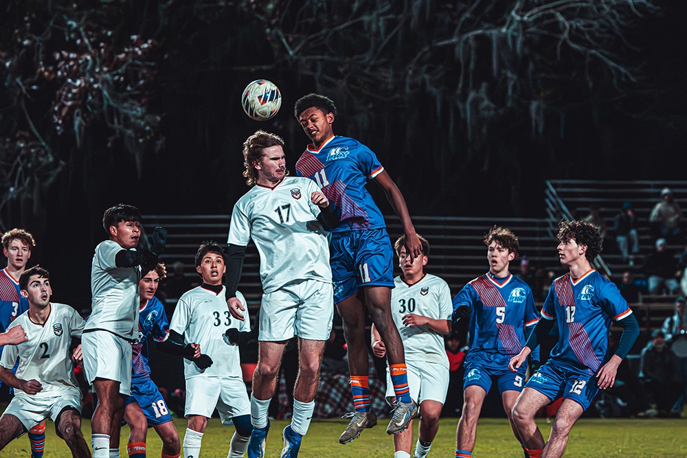 Soccer player heads a soccer ball while teammates watch